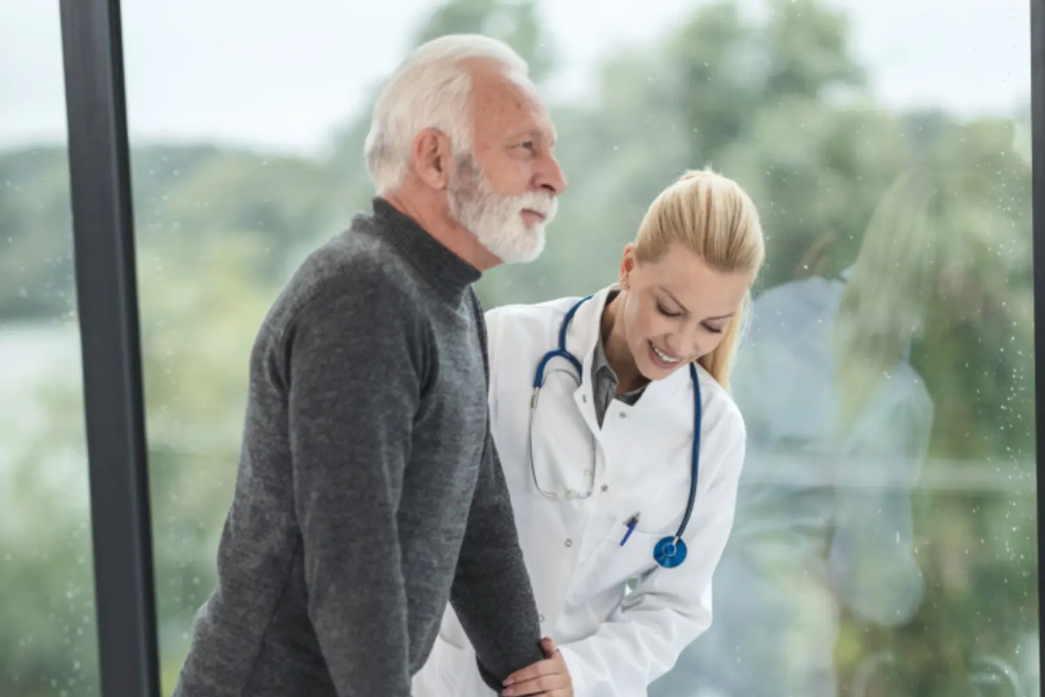 Profissional de saúde amparando um homem idoso pelo braço durante a caminhada